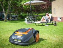 Vrouw ligt in tuinstoel terwijl robotmaaier gras maait